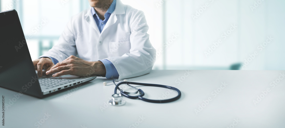 Doctor working on a laptop with a stethoscope on the desk